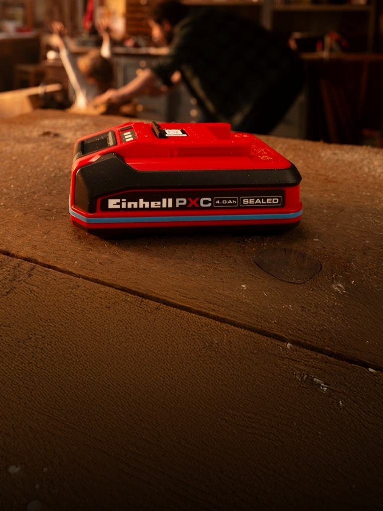 SEALED-technológiával készült 4,0 Ah-s Einhell Power X-Change akkumulátor egy fából készült munkapadon, kék gyűrűvel és könnyen beazonosítható címkével.