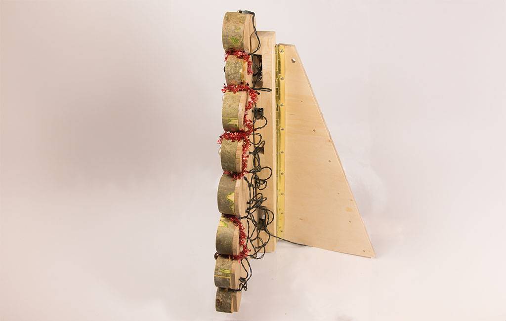Side view of the finished construction: wooden discs with string lights mounted on a wooden stand.