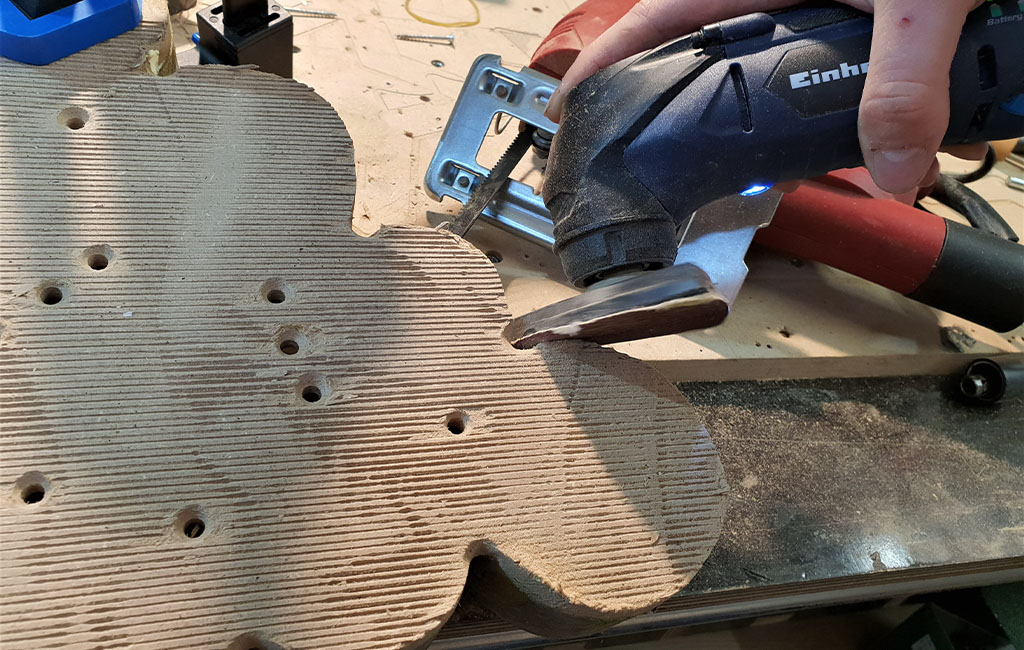 An Einhell multifunctional tool is used to cut a shaped wooden board with holes along the edges.