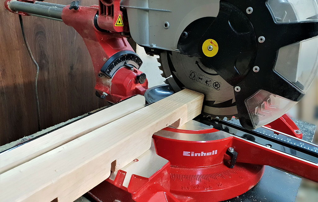 The Einhell sliding mitre saw cuts a rectangular wooden beam, close-up of the saw blade.