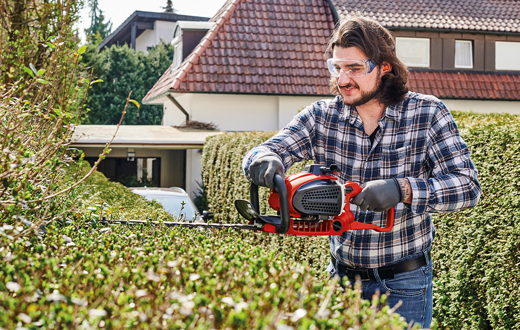 A man using the hedge trimmer for his bush.