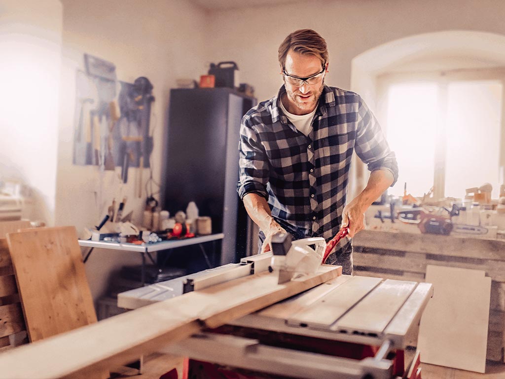 A man cutting a piece of wood with the Einhell table saw in his workshop.