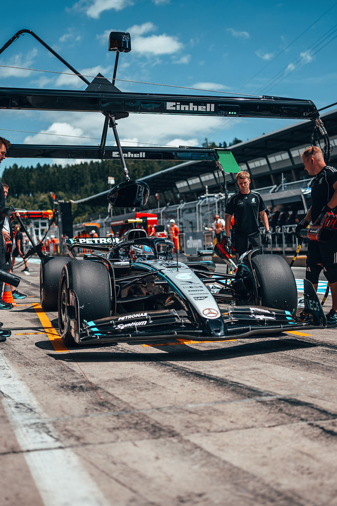 Egy Mercedes-AMG Forma-1-es autó a boxutcában, az Einhell garázs szerkezete alatt, a csapattagok körülvéve.