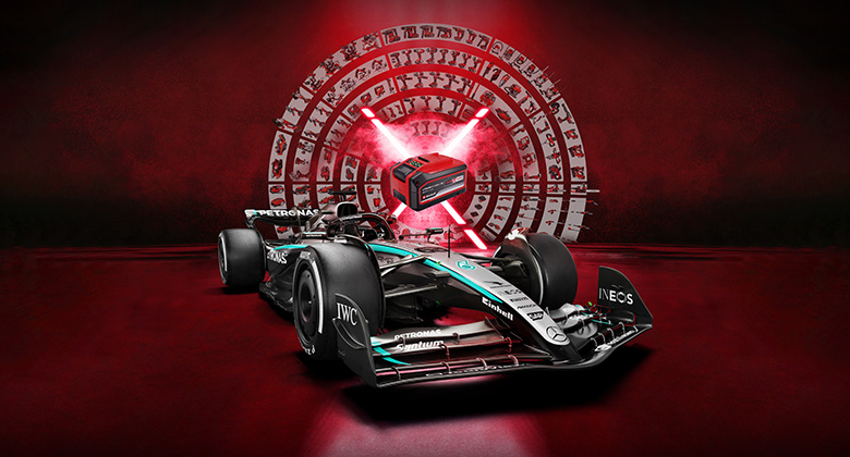 Élénkvörös háttér előtt álló Mercedes-AMG PETRONAS Forma-1-es autó, közepén egy Einhell akkumulátorral. Az Einhell és a Mercedes-AMG PETRONAS F1 Team logói a jobb alsó sarokban láthatók.