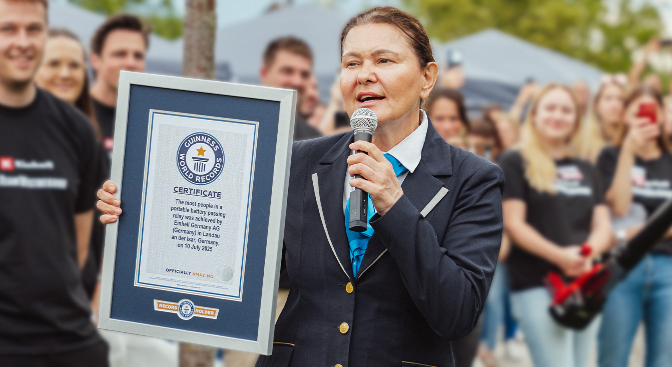 A GUINNESS WORLD RECORDS™ szervezetét képviselő, hivatalos ruházatot viselő nő tartja a kezében az Einhell akkumulátoros élőláncos-váltófutásos világcsúcsát igazoló oklevelet.