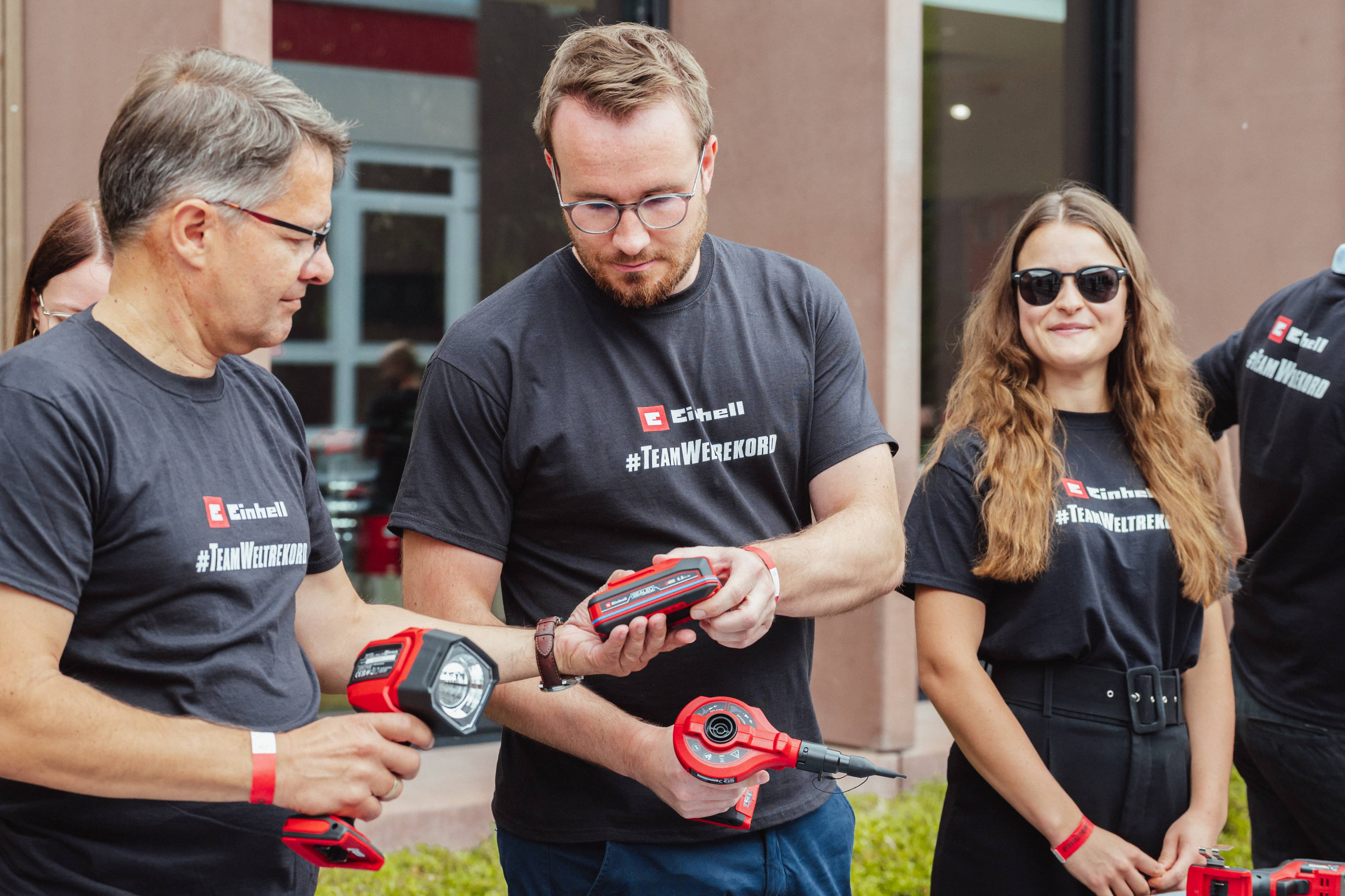 Three people in "#TeamWeltrekord" shirts examine an Einhell SEALED battery together.
