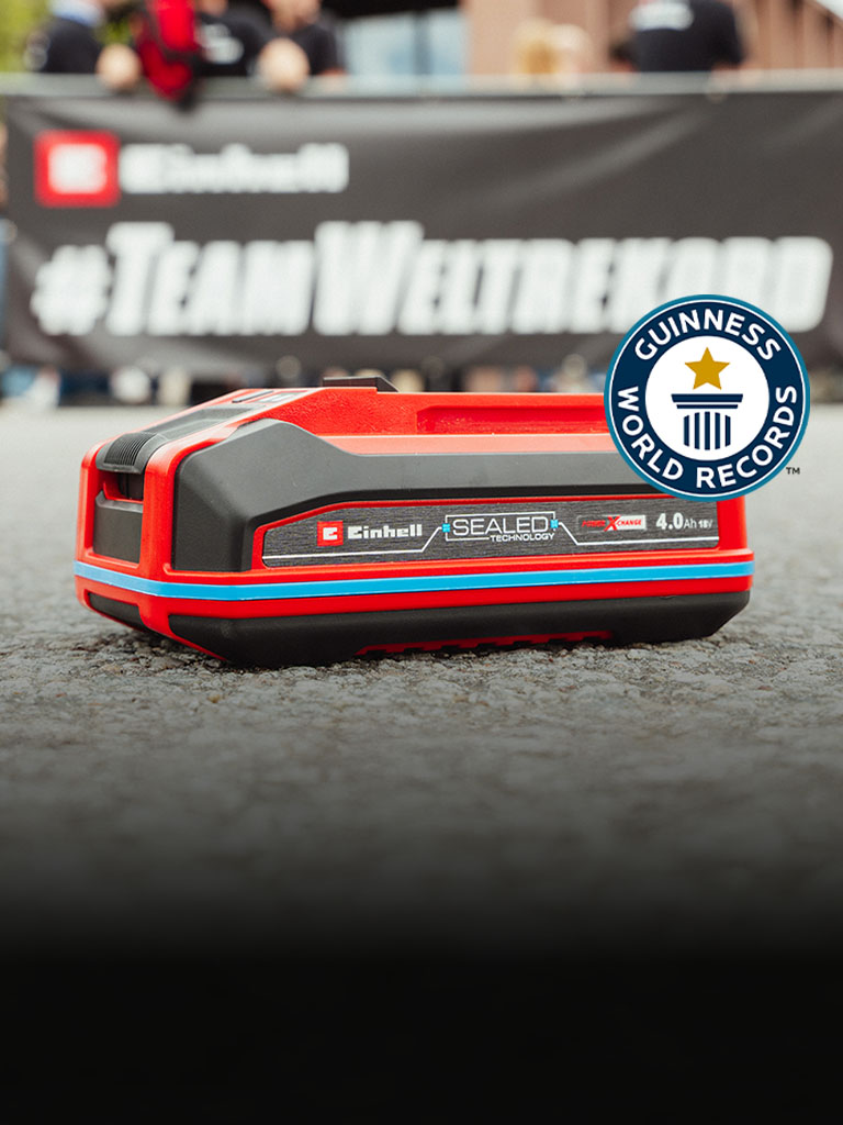 Az Einhell SEALED Power X-Change 4.0 Ah akkumulátor az aszfalton fekszik, a Guinness World Records „Record Holder” logóval a jobb oldalon.