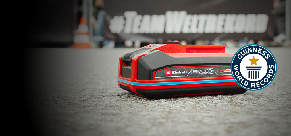 Az Einhell SEALED Power X-Change 4.0 Ah akkumulátor az aszfalton fekszik, a Guinness World Records „Record Holder” logóval a jobb oldalon.