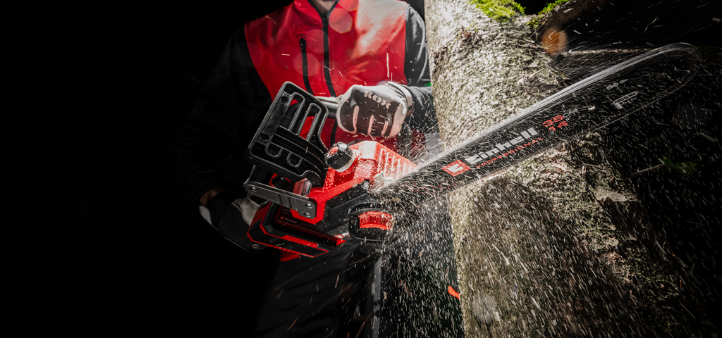 A man in red protective clothing saws into a tree with a chainsaw.